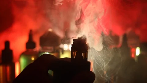 Smoke clouds and vape liquid bottles on dark background