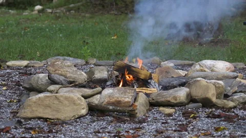 Smoke coming from a small, burning hot campfire that is surrounded by a ring of Stock Footage 342092046