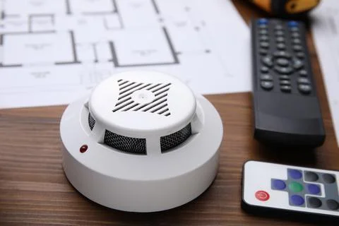 Smoke detector and remote controls on wooden table, closeup. Home security sy Stock Photos