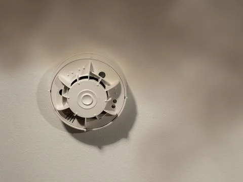 The smoke detector is installed on the ceiling and smoke rises underneath it. Stock Photos