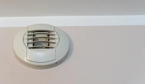 Smoke detector mounted on interior wall near ceiling, round white plastic Stock Photos