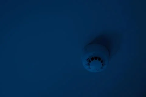 Smoke detector mounted on plain ceiling at dark nighttime Stock Photos
