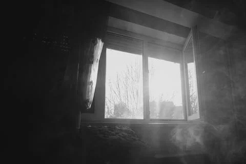 Smoke drifting across an open window in a dimly lit room with bright sunlight Stock Photos