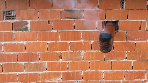 Smoke gently billows from a chimney attached to a rustic brick wall, 스톡 동영상 323376759
