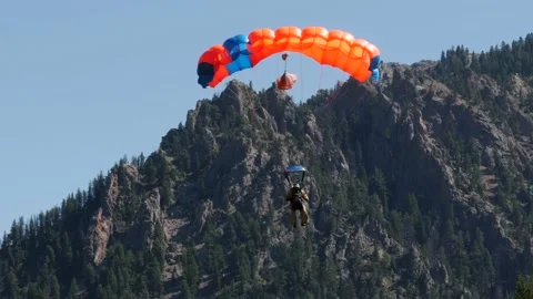 A smoke jumper is seen parachuting down into sage brush with a mountain in Stock Footage 131629313