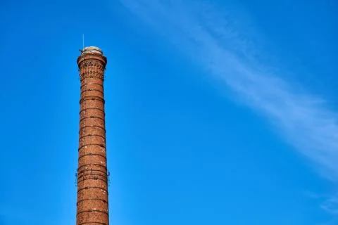 Smoke pipe made of bricks standing tall with white clouds and blue sky Stock Photos