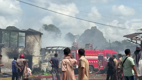 Smoke rises from burning structures. Firefighters near a red truck, hoses l.. Stock Footage 340742498