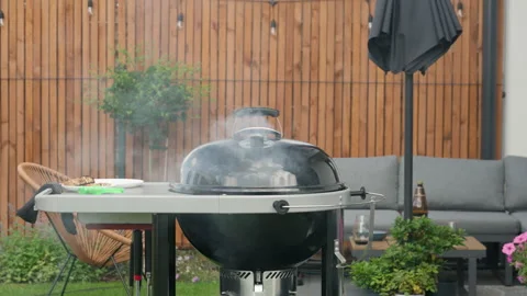 Smoke rises from a closed charcoal grill on an outdoor terrace during barbecue Stock Footage 340164112