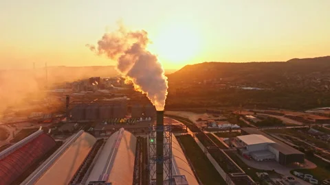 Smoke rises from a factory stack as the sun sets behind mountains in an 動画素材 341381245