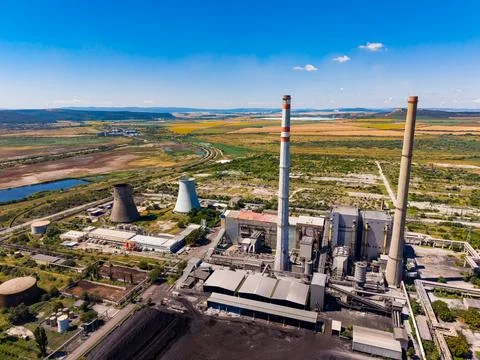 Smoke rises from industrial structures at a power plant near a green landsc.. Fotos Stock