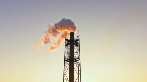 Smoke rises from a tall industrial stack against a clear sky during sunset in an 動画素材 340945511