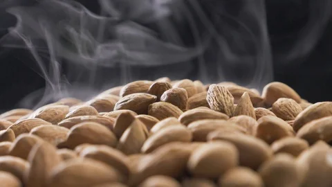 Smoke rises through almonds which spin on a black background Stock Footage 120083381