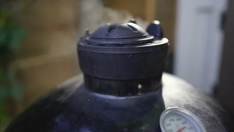 Smoke rises from the vent of a ceramic egg smoker Stock Footage 123300170