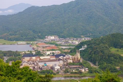 Smoke stack billows from small factory in rural mountain landscape 스톡 사진