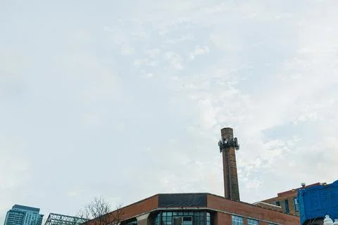 Smoke stack rises above urban buildings under a cloudy sky in a busy city 스톡 사진