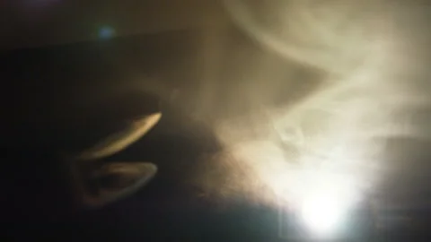 Smoke stream seeps through hole and reflects in light Stock Footage 92116603