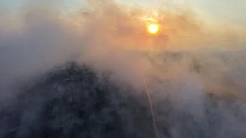 Smoke swirls around a sun setting over dark hills Stock Footage 333038432