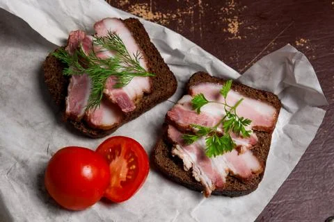 Smoked bacon with rye black bread and cuted tomatoes on the packaging paper. Stock Photos