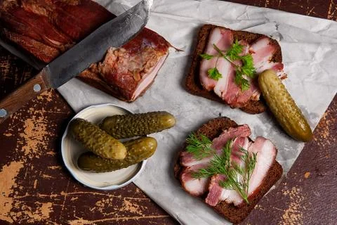 Smoked bacon with rye black bread and several pickles on the packaging pape.. Stock Photos