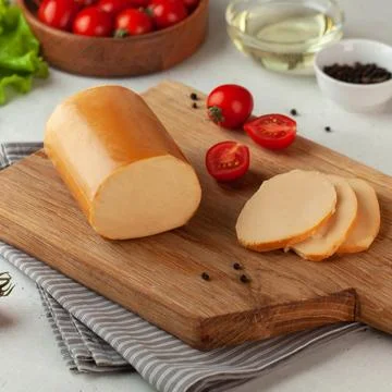 Smoked cheese log presented on a rustic wooden slice, styled with fresh tomatoes Foto stock