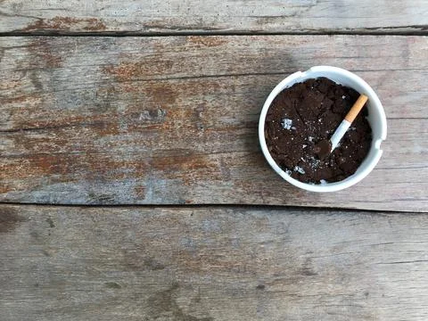 A smoked cigarette butt in a white ceramic ashtray full of used coffee grounds Foto stock