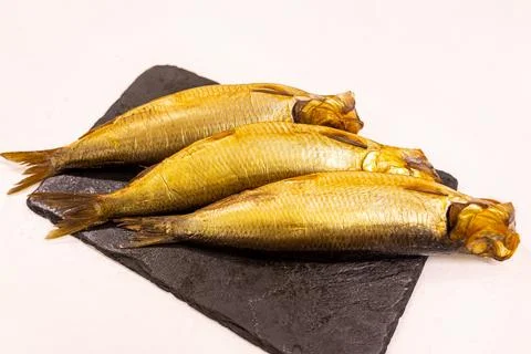 Smoked fish sit on a dark stone plate ready to be served in a simple kitche.. Stock Photos