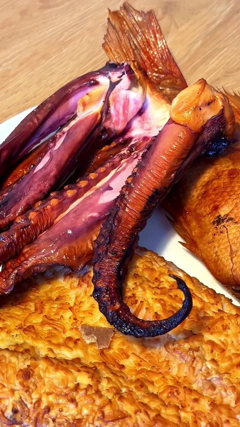 Smoked octopus tentacles and baked fish fillet arranged on white serving pl.. Stock Footage 337526331