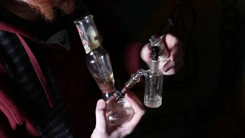 Smoker using glass bong pulls away from pipe and exhales into the darkness Stock Footage 146153951