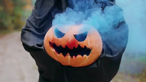 Smoking Jack O's lantern in the hands of an unknown man in a robe in the forest Stock Footage 253437762