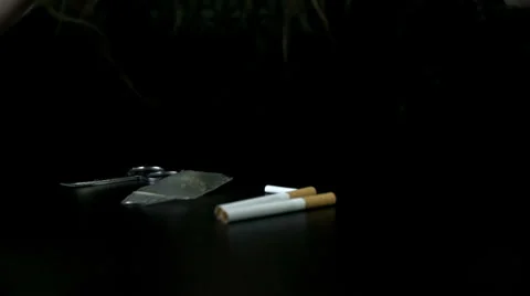 Smoking paper falls on the table next to two cigarettes on the black background Vídeos de archivo 33075145