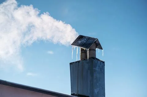 Smoking rooftop chimney with icicles on a cold winter day Stock Photos