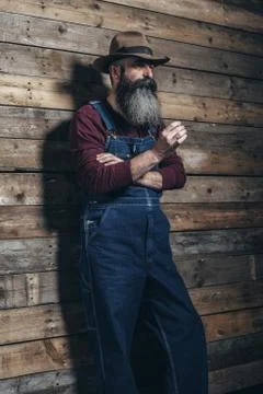 Smoking vintage worker man with long gray beard in jeans dungarees. Standing  Stock Photos