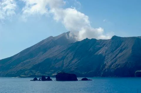 A smoking volcano, surrounded by ocean. Stock Photos