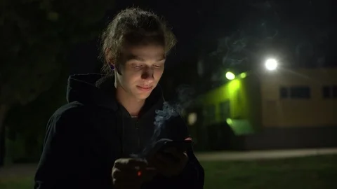 Smoking young man using smartphone at night on the street, 4k Видео 98879043