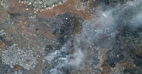 Smoldering dump site viewed from above with scavenging life amid the trash Stock Footage 95138736