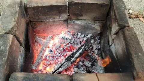 Smoldering firewood inside rustic brazier made from old bricks dirty with coa Stock Photos