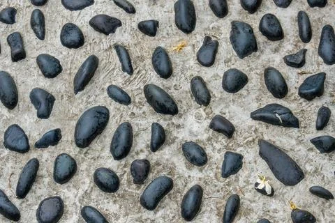 Smooth black pebbles scattered on sandy ground Stock Photos