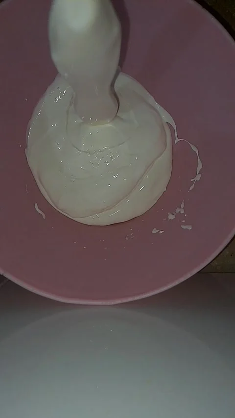Smooth cream pouring gracefully into a vibrant pink bowl Stock Footage 320386025
