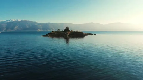 Smooth Fligth around very small island in calm sea with mountains in background Vídeo Stock 137850937