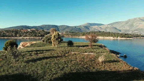 Smooth Fligth over very small island in calm sea with mountains in background Stock Footage 137851246