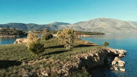 Smooth Fligth over very small island in calm sea with mountains in background Vídeo Stock 137851342