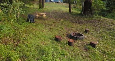 Smooth fly through of firepit towards small blue cabin in the woods Stock Footage 98272520