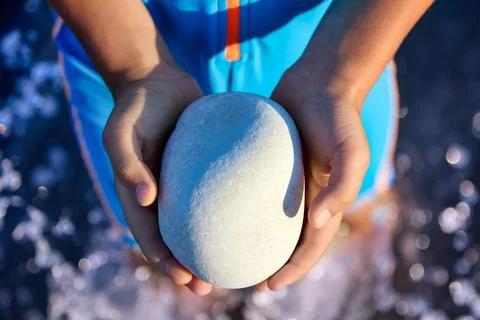 Smooth gray stone in the hands of a small child on the beach Stock Photos