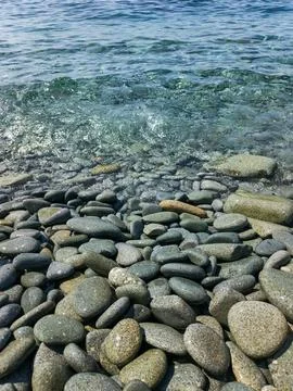 Smooth grey pebbles pattern on beach with transparent sea water 스톡 사진