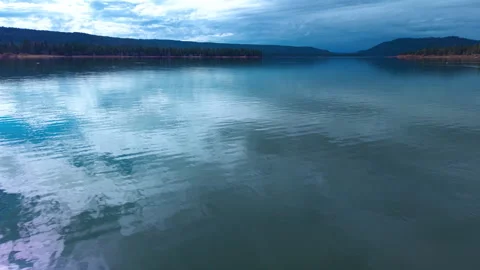 Smooth low altitude drone flyover across blue Lake with mountain silhouette Vidéo 328898795