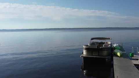 Smooth movement of pontoon boat and colorful kayaks docked at pier on calm lake Stock Footage 335776901