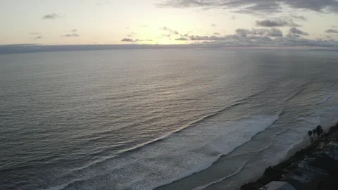 Smooth ocean waves move toward sleepy beach town at sunset Stock Footage 167677082