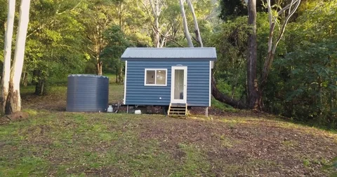 Smooth pull away from small blue cabin in the woods through foilage Stock Footage 98272933