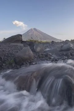 Smooth river motion over dark rocks with Mount Semeru  in the background. Fotos Stock