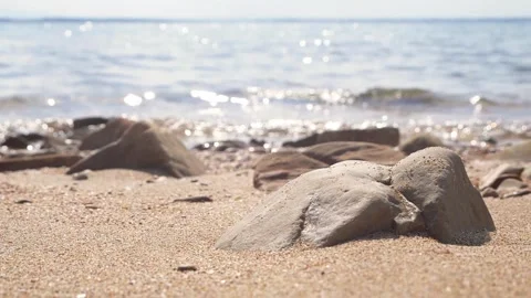 Smooth rocks rest on a sandy beach with shimmering ocean. Stock Footage 337406544